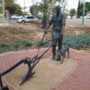 Bronze sculpture of a man with a plow and a dog in an outdoor setting. Sculptor - Robert C Hitchcock
