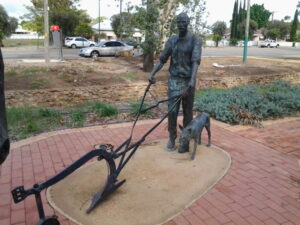 Bronze sculpture of a man with a plow and a dog in an outdoor setting. Sculptor - Robert C Hitchcock