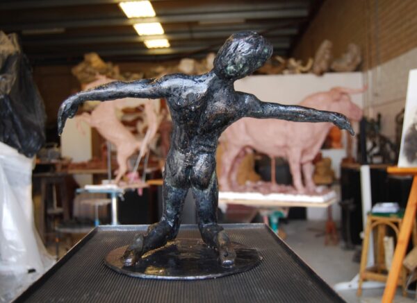 Bronze sculpture of a humanoid figure in a dynamic pose displayed in an artist's studio. Sculptor - Robert C Hitchcock