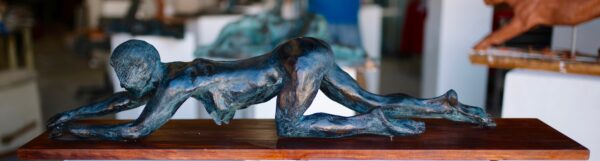 Bronze sculpture of a crawling figure displayed on a wooden base. Sculptor - Robert C Hitchcock