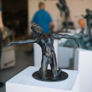 Bronze sculpture of a figure with outstretched arms on display, with viewers in the background. Sculptor - Robert C Hitchcock