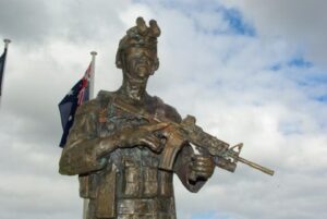 Bronze sculpture of a soldier with a rifle, set against a cloudy sky with flags in the background. Sculptor - Robert C Hitchcock