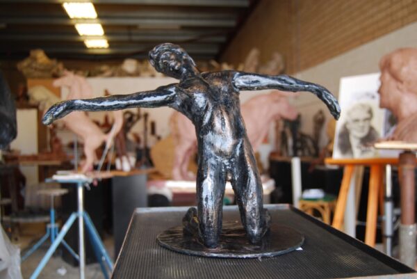 A bronze sculpture of a figure with arms outstretched on display in an art studio. Sculptor - Robert C Hitchcock