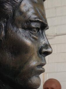 Close-up of a bronze sculpture's face profile with a blurred background. Sculptor - Robert C Hitchcock