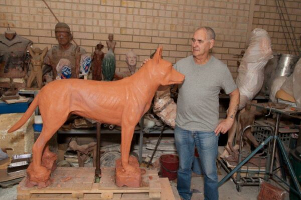 Sculptor evaluating a life-sized bronze sculpture of a dog in a workshop. Sculptor - Robert C Hitchcock