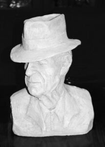 Black and white photo of a bronze sculpture bust of a man wearing a fedora hat. Sculptor - Robert C Hitchcock